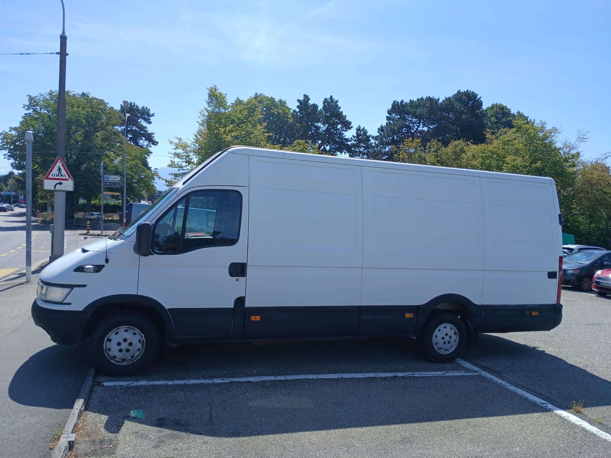 Fourgon utilitaire blanc stationné de profil sur un parking, avec des arbres en arrière-plan